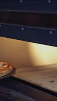 Hot delicious pizza. Pizzeria master takes out ready pizza from the oven. Chef is pulling out fresh pizza with a special pizza spatula in the kitchen. Vertical video