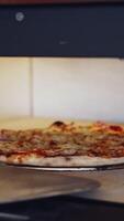 Pizza is getting ready in oven. Chef opening oven door and checking pizza readiness. Cook checks pizza for readiness using the pizza ring. Vertical video