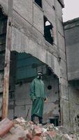 Survivor in safety suit in ruined place. Man in gas mask and protective wearing standing alone in abandoned place. Post-apocalyptic concept. Vertical video