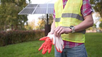 Engineer on workplace puts on protective gloves while standing in front of solar panel. Technician wearing work gloves in front of sun panels. Green clean energy. Worker putting on work gloves. video