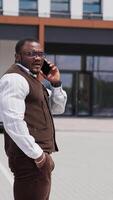 Handsome office manager speaking on mobile phone outdoor and smiling. Looking confident and having important conversation. Serious man wearing stylish formal clothes Vertical video