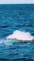 Amazing water background. Waves swaying on the sea water. Beautiful blue water waves with white foam crashing on the dock. Slow motion. Vertical video