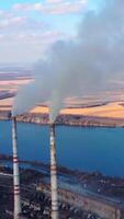 View from the drone at the old aged weathered tall industrial factory chimney with smoke over it. Cloudy sky background Vertical video