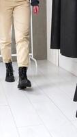 Unknown woman comes up to a high stool and sits down. Model demonstrates stylish boots from combined leather. White backdrop. Vertical video