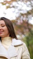 Beautiful smiling Caucasian lady speaks on the phone walking by the park. Lady goes looking at phone and then tries to take a picture of autumn trees. Vertical video