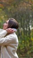 Enjoying walk in the nature and beautiful autumn weather. Brunette raising the collar of her jacket and smiling into camera. Vertical video