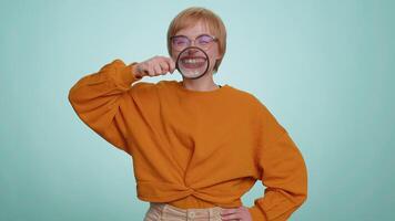 Woman holding magnifier glass loupe on teeth, looking at camera showing funny smiling face mouth video