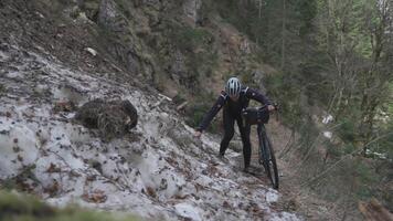Man cyclist pulls bicycle through avalanche in mountains. Bicyclist is trapped in obstacle and is pulling his cycle through an ice slide with bicycle in his hands. Avalanche on cycling route in Alps. video