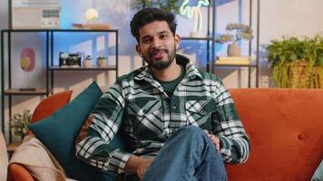 Indian man smiling friendly at camera, waving hands gesturing hello, hi, greeting at home on sofa video