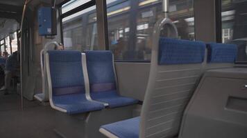 Interior of a moving tram in Munich, Germany, showcasing empty seats. The design of the tram seats and the bustling cityscape outside highlight the experience of public transportation in the city. video
