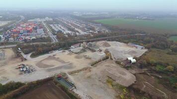 Aerial view of active sand quarry in Germany, surrounded by industrial zones. Heavy machinery operates in foggy autumn atmosphere, emphasizing raw, industrial landscape and ongoing extraction work. video