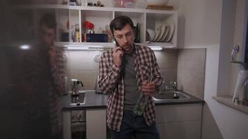 A young, sad, and depressed man stands in his kitchen, holding a bottle of wine. Battling personal and work problems, he talks on the phone, facing alcoholism, emotional struggles, and inner turmoil. video