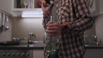 A young, sad, and depressed man stands in his kitchen, holding a bottle of wine. Struggling with personal and work problems, he talks on the phone, facing alcoholism and emotional despair. video
