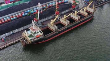 Bulk carrier is loaded with coal in the port using cranes. Drone view video