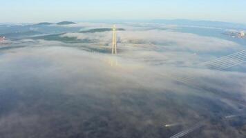 Cable-stayed bridge spanning a foggy strait in a dawn aerial view video