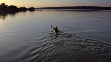 Young man kayaks on lake at sunset. Alone man riding on a rowing boat on the lake at dusk time. Man in a boat with oars in the evening. Aerial view. video