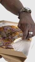 Delicious pizza in black man's hands. African man holds a box with delivered pizza and trying to eat some slice. Unhealthy food. Close-up. Slow motion. Vertical video