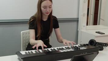 Young music composer engaging with an electronic piano keyboard, tablet, and headphones in a home studio, creating and refining original melodies and harmonies video