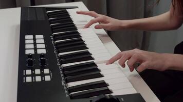 Close up view of a female musician skillfully playing a midi keyboard, featuring pads and knobs, while composing electronic music in a modern home studio setting video