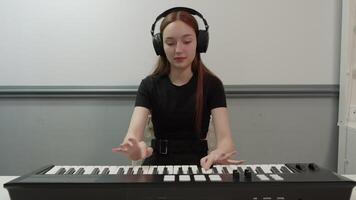 Young female music composer wearing headphones playing and composing music on a synthesizer at home in her studio, she is focused and inspired, creating new melodies video