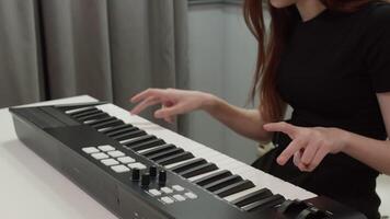 Female musician playing a midi controller keyboard, composing electronic music in a home studio setting, utilizing modern technology for music production video