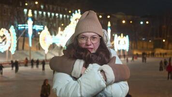 Beautiful young woman froze while skating at ice rink in evening, despite her warm clothes, she tries to keep warm by frowning and hugging herself video