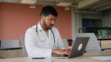 Indian doctor working on a laptop in a modern workspace video