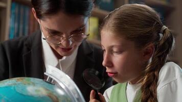 Professor female Caucasian professional tutor woman teacher explaining discuss teaching educating little girl school child kid student learner studying globe earth world map use magnifier in classroom video