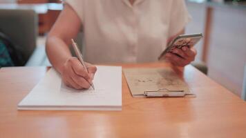 The Power of Note-Taking. A close-up shot of a woman's hands diligently writing in a notebook while holding a smartphone, showcasing the multitasking nature of modern life. video