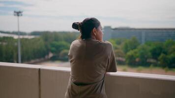 Contemplation on the Balcony. A woman stands alone, gazing out over a cityscape, her back to the camera. The image evokes a sense of introspection and quiet contemplation. video