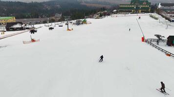 A skier descends a snowy slope with nearby chairlifts and a winter resort surrounded by forested hills. video