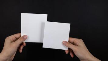 Two blank white cards held in hands against black background. photo