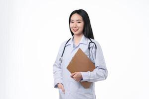 Young asian female doctor in uniform and stethoscope smiling and looking at camera while standing with clipboard in hands on white background. Healthcare and medical concept. photo