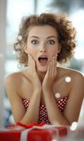 A young woman displays a joyful expression with wide eyes and a surprised smile while touching her face in a festive setting. Colorful decorations suggest a celebration photo