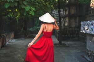 A tourist in a red dress and a traditional Vietnamese hat in the garden of a pagoda in Asia photo