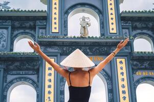 Female tourist in a traditional Vietnamese hat on the background the gate to Chua Linh Ung Pagoda in Danang in Vietnam photo