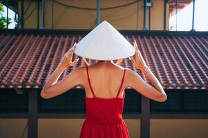 A tourist in a red dress and a traditional Vietnamese hat against the background of a tiled roof in Asia photo