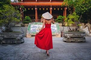 Tourists in a red dress and a traditional Vietnamese headdress in the shape of a cone against the backdrop of a pagoda in Nha Trang photo