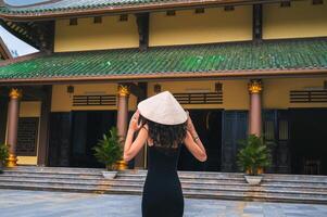 Chua Linh Ung in Da Nang, Vietnam. A female tourist wearing a traditional Vietnamese Non La hat on the background of a pagoda. photo