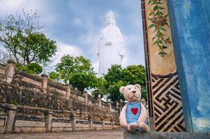 A traveler's bear toy on the background and White Lady Buddha with blue sky at Chua Linh Ung Bai But Temple, Da Nang, Vietnam. photo