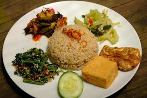 Nasi Campur Vegetarian is is brown rice with sauted green vegetables, sambal, sliced cucumber and tomato slices, fried tofu, and fried tempeh. Suitable for vegetarians. Indonesian food. Nasi Rames. photo
