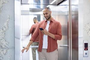 A young man wearing casual attire checks his smartphone while entering an elevator. The scene emphasizes modern technology usage in everyday activities. photo