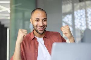Man close up celebrating successful achievement results, employee received online email notification. Joyfully holding hands up in triumph gesture. photo