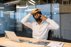 An office worker puts drops in his eyes to relieve pain from long hours of work at a computer and laptop. A man works until late at his workplace inside the office. photo