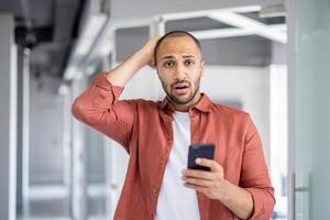 Man reacting in surprise to a notification on his smartphone with startled expression. photo