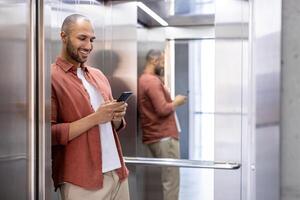 Man standing in elevator using smartphone, leaning against mirror wall, smiling effortlessly, dressed in casual attire. Scene depicts connectivity, communication, modern technology, daily routine. photo