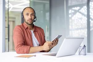 Confident customer service representative wearing a headset and using a tablet while working. Displays professionalism, modern technology usage, and business communication in a contemporary office photo