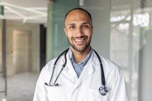 Portrait of a cheerful doctor in a clinic setting, portraying professionalism, confidence, and approachable patient care, wearing a white coat and stethoscope, and standing indoors with a warm smile. photo
