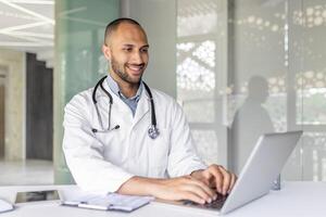 A smiling doctor is using a laptop in a modern office setting, showcasing productivity and professionalism. The image captures a sense of technology integration in the healthcare field. photo