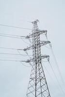 A tall High Voltage Power Line Tower rises against a slightly overcast sky with clouds photo